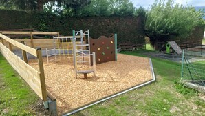 Een speeltuin met een houten klimstructuur, een glijbaan en een omheind gebied.