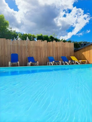 A swimming pool with blue lounge chairs and a wooden fence in the background.