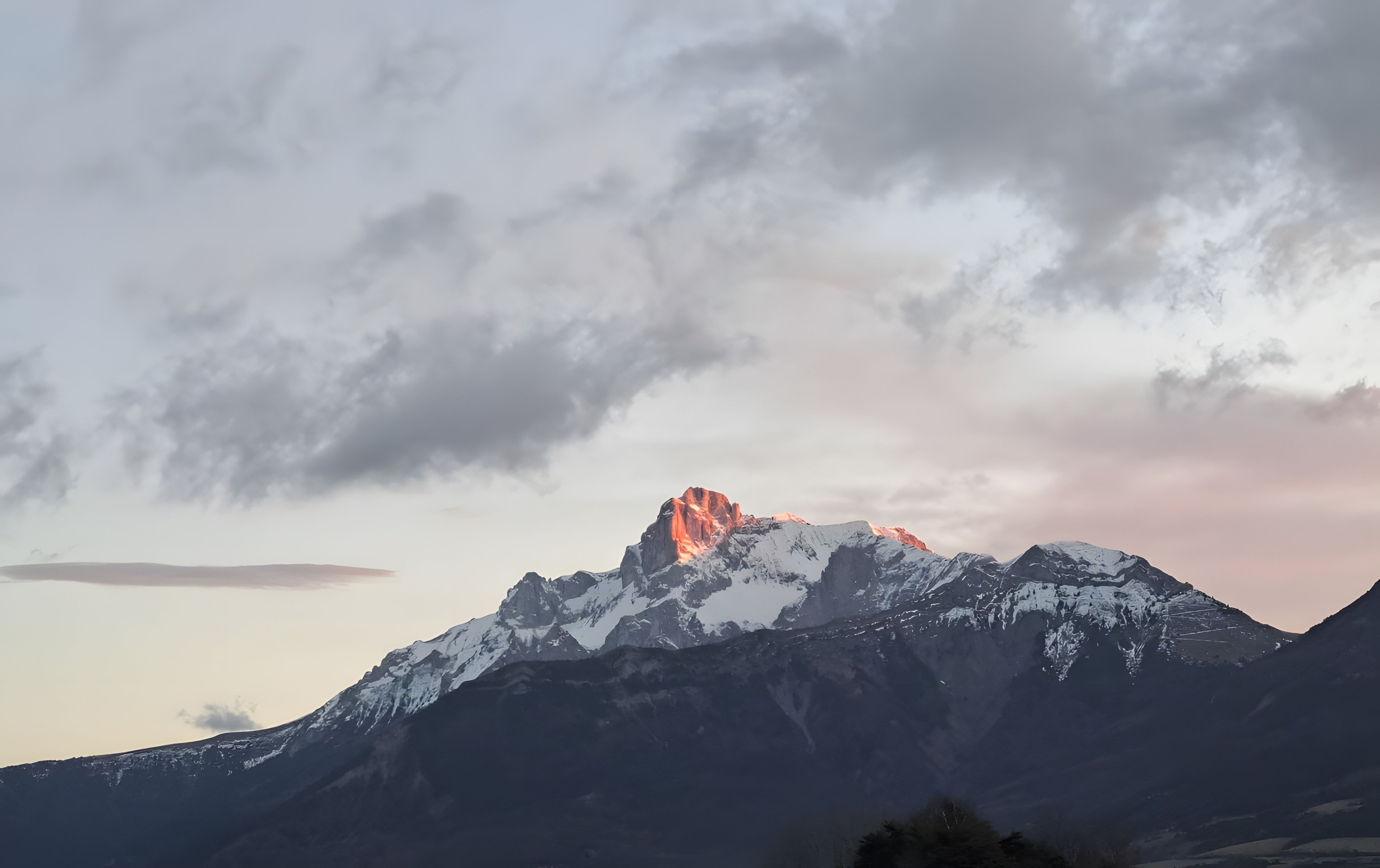 A mountain range with snow-covered peaks and a prominent peak with a reddish glow.