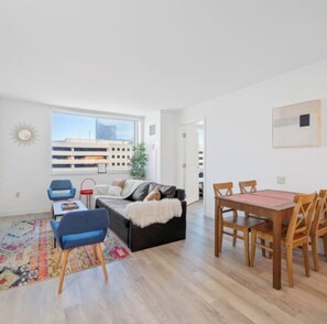 A modern living room with a sofa, a dining table with chairs, a small coffee table, a rug, and a window with a view of buildings. - 2 bedroom apt, with water park, on the Boardwalk (Atlantic City)