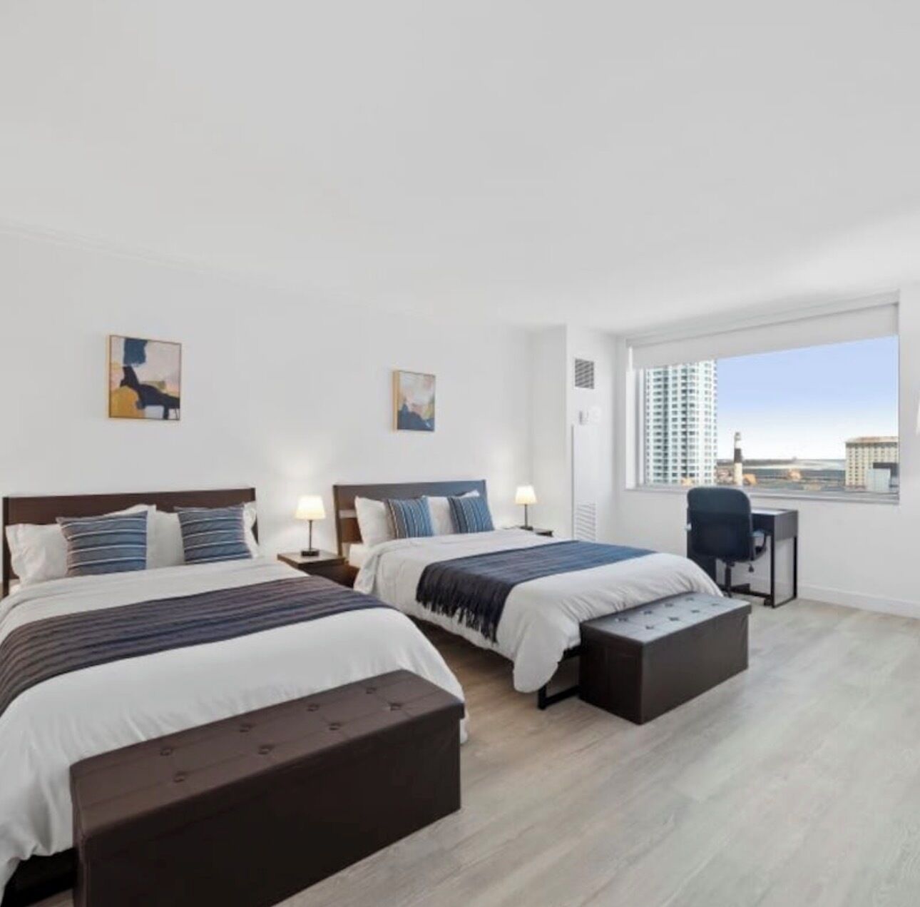 Ett modernt hotellrum med två sängar, ett skrivbord och ett stort fönster med utsikt över staden.