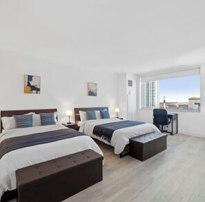 A modern hotel room with two beds, a desk, and a large window with a city view. - 2 bedroom apt, with water park, on the Boardwalk (Atlantic City)