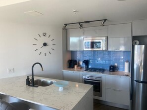Una cocina moderna con microondas integrado, electrodomésticos de acero inoxidable, un reloj y una encimera de mármol.