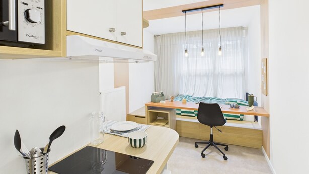 A modern kitchen with a built-in stove, a dining area with a wooden table and chairs, and a window with sheer curtains.