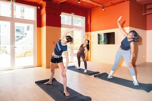 A fitness class in a room with large windows, wooden floors, and orange walls.