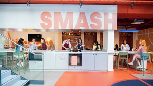A modern kitchen area with a central island, seating arrangements, and a large 'SMASH' sign above.