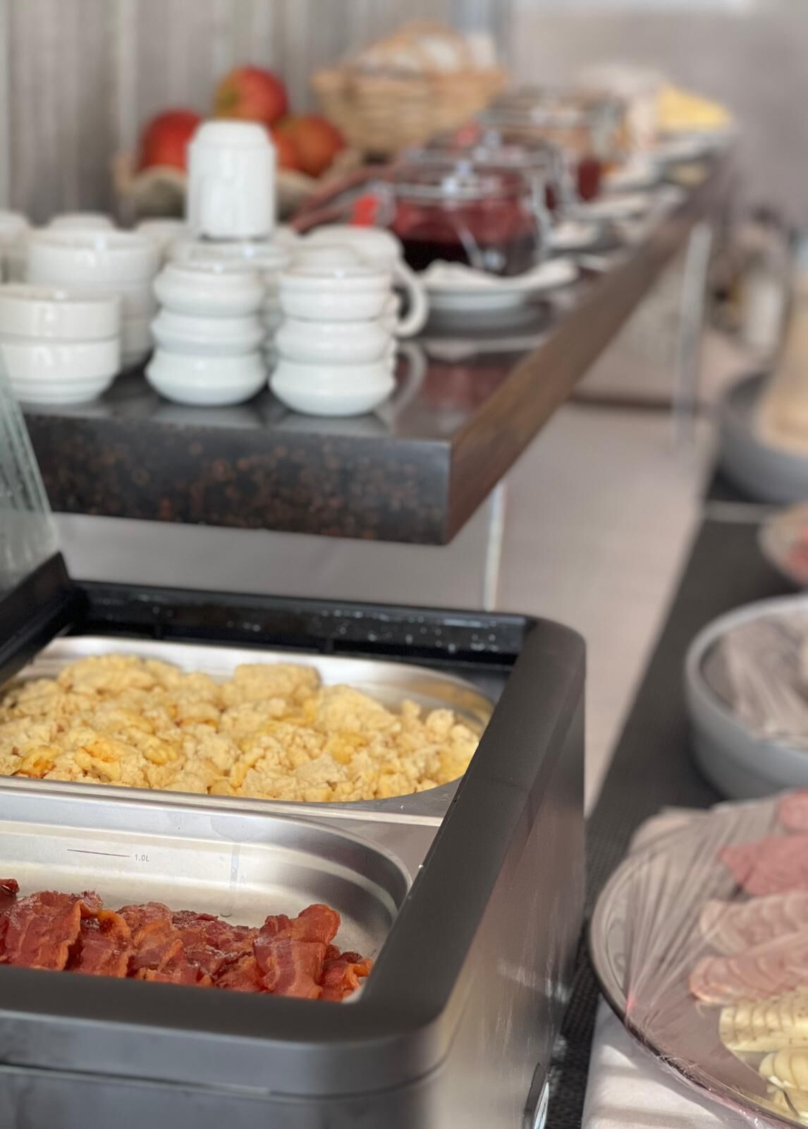 Un bufé con diversos alimentos, entre ellos huevos revueltos, tocino y una variedad de salsas.
