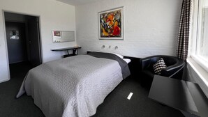 A hotel room with a bed, a desk, a chair, a painting on the wall, and a window with curtains. - Hotel Lakolk (Rømø)