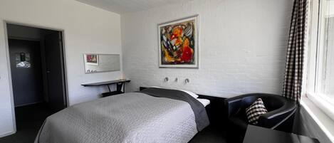 A hotel room with a bed, a desk, a chair, a painting on the wall, and a window with curtains.
