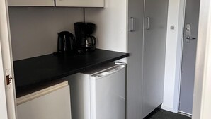 A compact kitchen with white cabinets, a black countertop, and a built-in dishwasher. - Hotel Lakolk (Rømø)