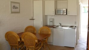 A compact kitchen with white cabinets, a microwave, a coffee maker, and a sink. There is a dining table with four wicker chairs. - Hotel Lakolk (Rømø)