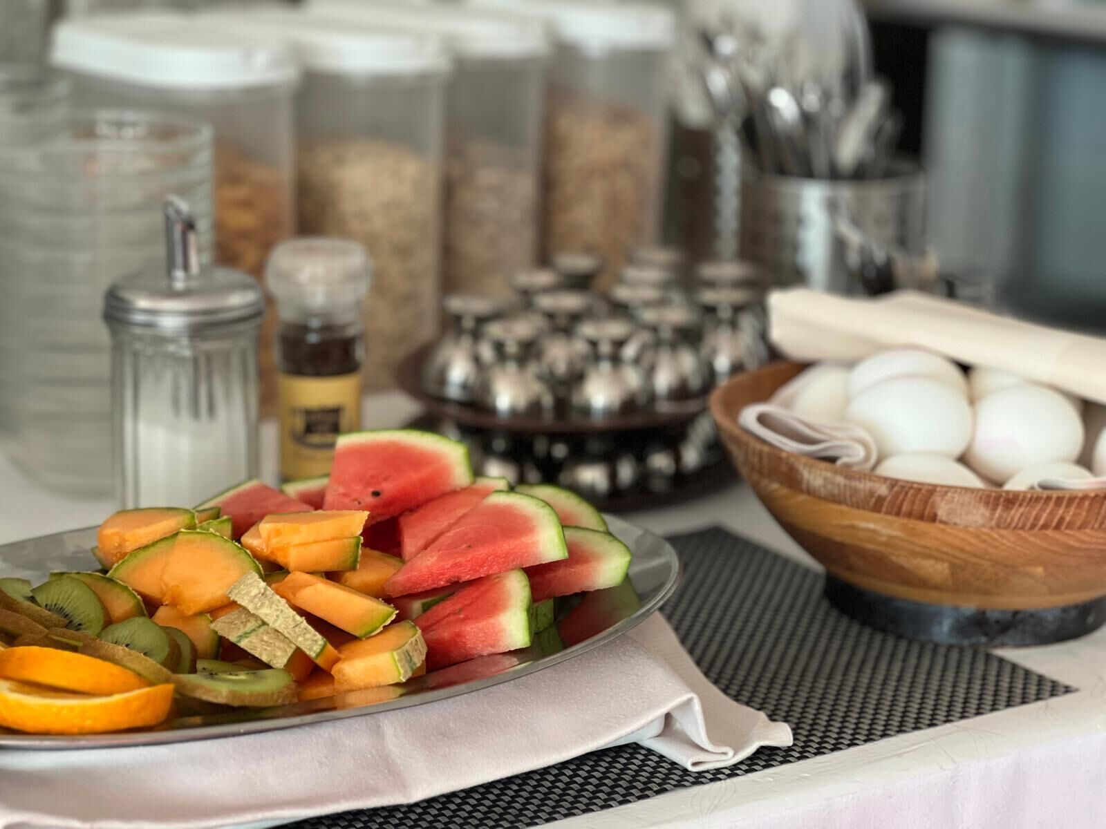 A table with a fruit platter, a bowl of eggs, and kitchen utensils.