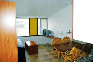 Una habitación con una mesa de comedor, sillas, televisor y una ventana con persianas.