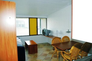A room with a dining table, chairs, a television, and a window with blinds.