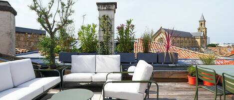 A rooftop patio with outdoor seating, a stone wall, and a view of a church with a bell tower.