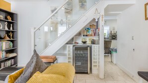 Un interior moderno con una escalera, una zona de cocina y un espacio de estar con sofá y estanterías.
