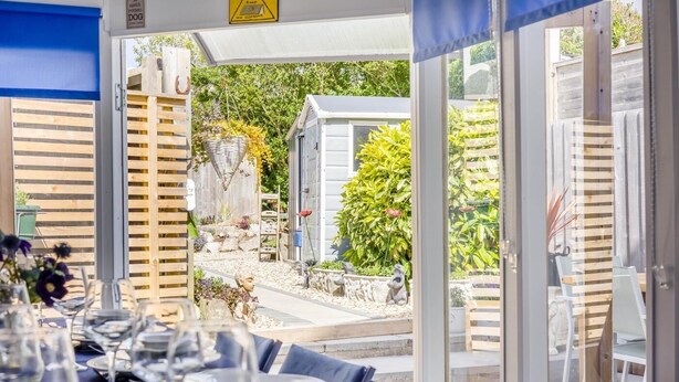 Un área de comedor al aire libre con mesas dispuestas para una comida, una valla de madera y vista a un jardín.