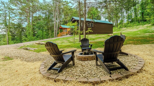 Een blokhut met een vuurkuil en Adirondack-stoelen in een bosrijke omgeving.