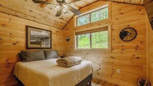 Een slaapkamer in een houten blokhut, met een bed, een plafondventilator, een raam en een klok met berenmotief.