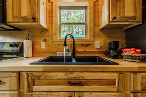 A kitchen with wooden cabinets, a window, a sink, a coffee maker, and a basket of snacks.
