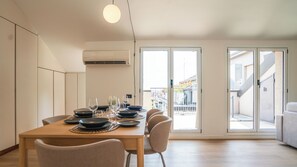Zona pranzo moderna con tavolo in legno apparecchiato per sei persone, un'ampia finestra e vista su un edificio con balconi.