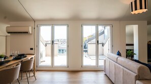 Um espaço de estar moderno com área de jantar, sofá e grandes portas de vidro deslizantes que dão para um terraço ao ar livre.
