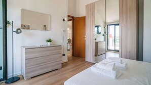 Ein modernes Schlafzimmer mit einem hölzernen Schminktisch, einem Bett mit weißer Bettwäsche, einem großen Spiegel und Blick auf den Balkon.