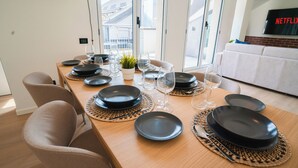 Ein Essbereich mit einem langen Tisch, gedeckt für eine Mahlzeit, einem Fernseher im Hintergrund und Blick durch das Fenster.
