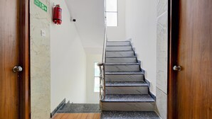 A staircase with a fire exit sign, a fire extinguisher, and a window at the top. - Classic Hotel Gandimaisamma (Hyderabad)