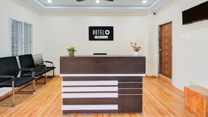 A hotel reception area with a reception desk, a ceiling fan, a waiting area with chairs, and a wooden floor. - Classic Hotel Gandimaisamma (Hyderabad)