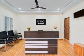 A hotel reception area with a reception desk, a ceiling fan, a waiting area with chairs, and a wooden floor. - Classic Hotel Gandimaisamma (Hyderabad)
