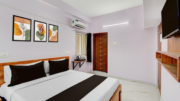 A bedroom with a bed, a TV, a window with a curtain, and wall art. - Classic Hotel Gandimaisamma (Hyderabad)