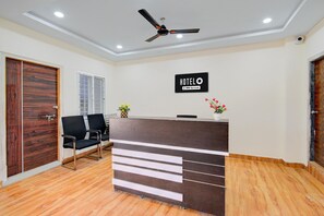 A hotel reception area with a reception desk, black chairs, a ceiling fan, and a sign indicating the hotel is serviced by OYO.