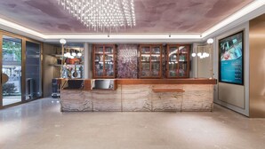 Eine moderne Hotelhalle mit einer Marmor-Rezeption, Bücherregalen und einem digitalen Bildschirm, der Informationen anzeigt.