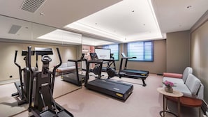 Ein moderner Fitnessraum mit Laufbändern, Spiegelwand und einer Sitzecke mit Blumen.'