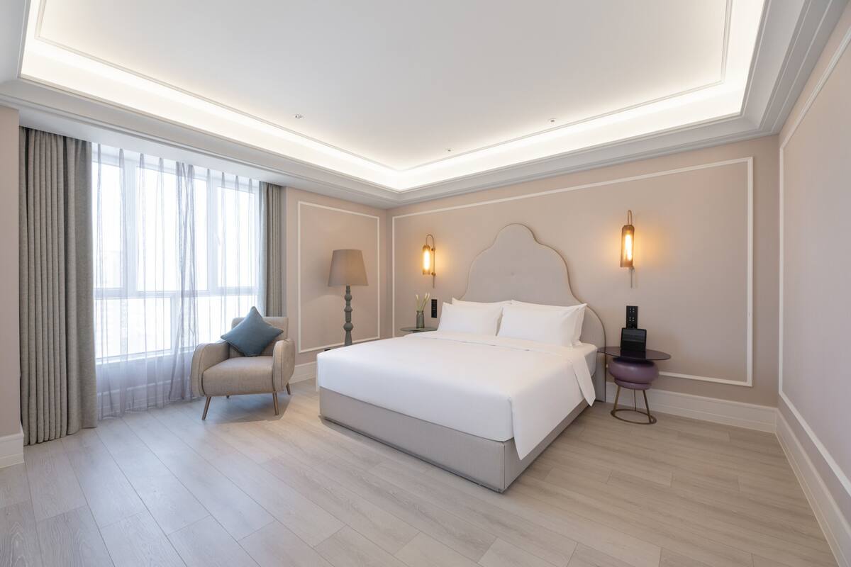 Una habitación de hotel moderna con una cama grande, una silla, una mesita de noche y una lámpara.