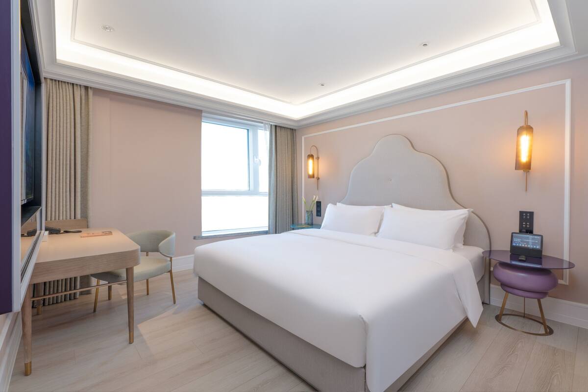 Una habitación de hotel moderna con una cama grande, un escritorio, una silla, una mesita y una mesita de noche con una lámpara.