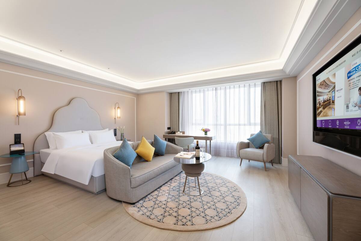 Una habitación de hotel moderna con cama, sofá, mesa de centro, televisor y un rincón de comedor.