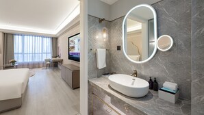 Un baño de hotel moderno con un espejo ovalado grande, un lavamanos blanco y una pared de mármol.