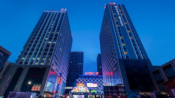 Dos edificios altos con señalización iluminada, un edificio central con una gran pantalla digital, y cielo despejado.
