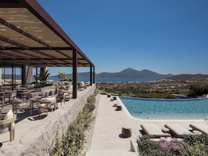 A rooftop terrace with outdoor seating, a swimming pool, and a view of the sea and mountains. - ONERO (Milos)