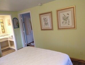 Une chambre à coucher comprenant un lit, un bureau et deux reproductions botaniques encadrées accrochées au mur.