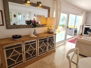 A living room with a large mirror, a wooden console table with decorative items, a sofa, and a view through a glass door to an outdoor area. - Villa Buena Vista, pool and seaviews (AN)