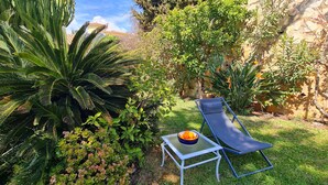 Un jardin avec un fauteuil de relaxation, une table sur laquelle se trouve un saladier rempli de fruits, et diverses plantes.