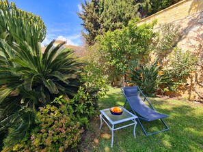 A garden with a lounge chair, a table with a bowl of fruit, and various plants. - Villa Buena Vista, pool and seaviews (AN)