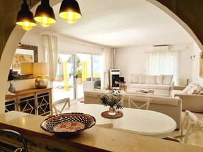 A living room with a white sofa, a dining table with a decorative bowl, and a TV. - Villa Buena Vista, pool and seaviews (AN)