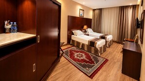 Habitación de hotel con dos camas, un armario de madera, un escritorio, un televisor y un tapete rojo estampado.