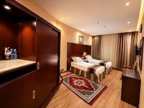 A hotel room with two beds, a wooden wardrobe, a desk, a TV, and a red patterned rug. - Premium Land 1 (Makkah)