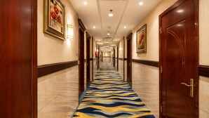 Un pasillo de hotel con alfombra estampada, puertas de madera y cuadros en las paredes.
