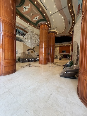 A spacious lobby with marble flooring, large wooden columns, a grand chandelier, and a seating area with massage chairs. - Premium Land 1 (Makkah)
